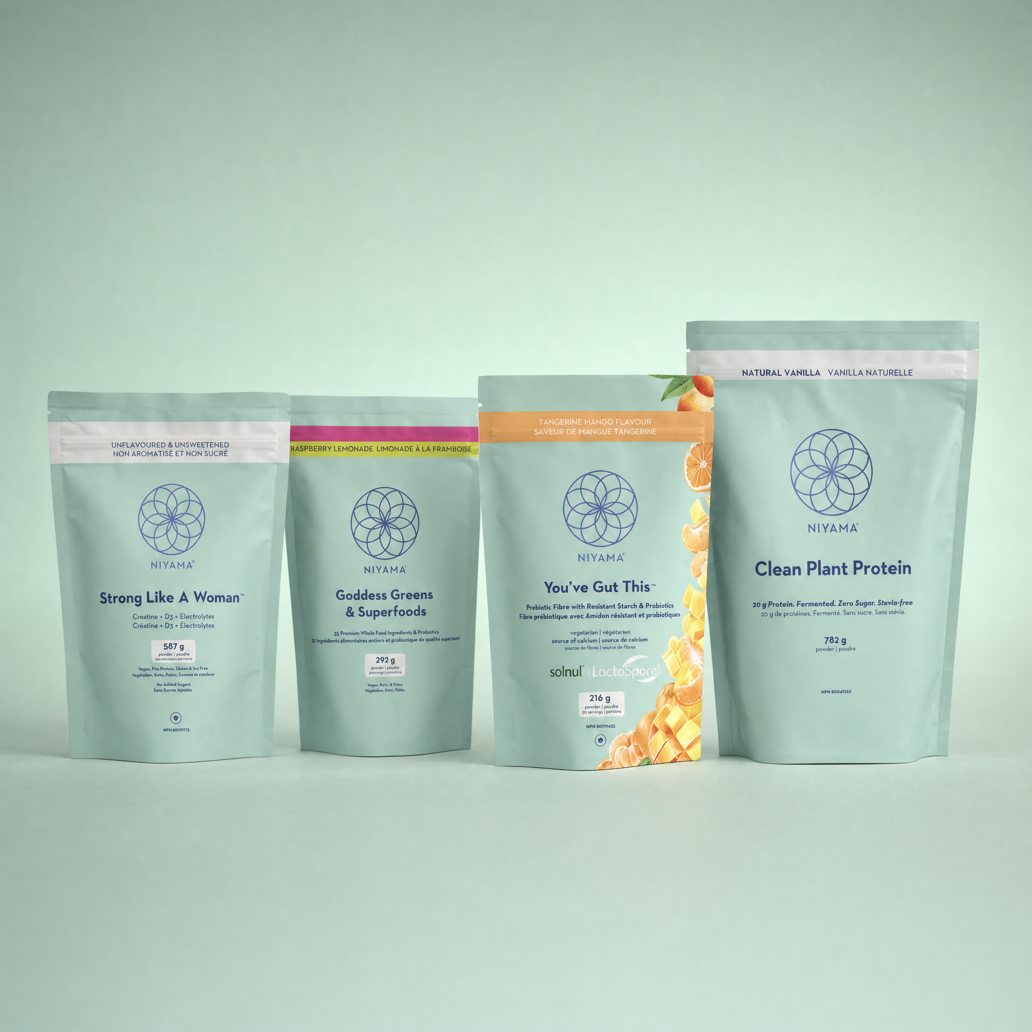Four stand-up pouches of Niyama in different flavors and protein types, arranged in a row against a solid pale mint green background. The pouches are light blue-green with different colored accent bands (pink, magenta, orange, and white) Strong Like A Woman, Goddess Cream & Superfoods, You're Got This, and Clean Plant Protein.